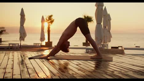 Ein-Junger-Mann-Macht-Morgens-Yoga-An-Einem-Sonnigen,-Mit-Brettern-Bedeckten-Strand.-Ästhetische-Perspektive-Auf-Yoga