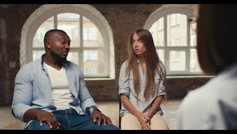 A-guy-with-Black-skin-in-a-blue-shirt-talks-with-a-blonde-girl-in-a-blue-shirt-and-a-psychologist.-International-couple-at-an