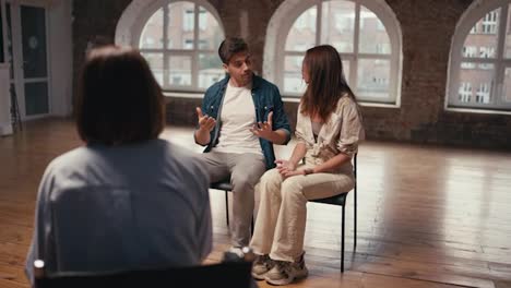 A-couple-at-a-reception-with-a-psychologist:-a-brunette-girl-and-a-brunette-guy-in-a-denim-jacket-who-expressively-talks-about-their-dissatisfaction.-Couple-therapy-with-a-psychologist