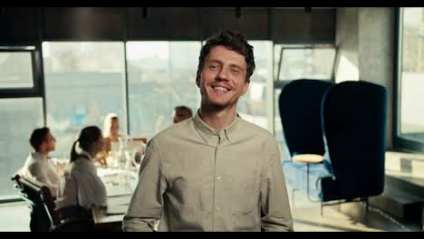 Happy-guy-office-worker-in-a-white-shirt-posing-in-the-office-against-the-background-of-his-colleagues