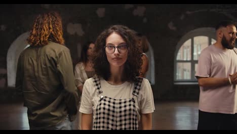 Portrait-of-a-brunette-girl-with-curly-hair-in-round-glasses-who-poses-at-group-therapy-in-a-brick-building.-Solving-your-problems-and-complexes-in-group-therapy