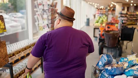 Rear-view:-An-overweight-man-in-a-purple-T-shirt-and-a-brown-hat-walks-through-the-store-and-looks-at-the-products