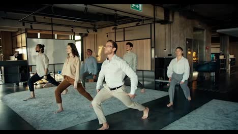A-man-in-a-white-shirt-and-glasses-is-doing-yoga-with-his-colleagues-in-the-office
