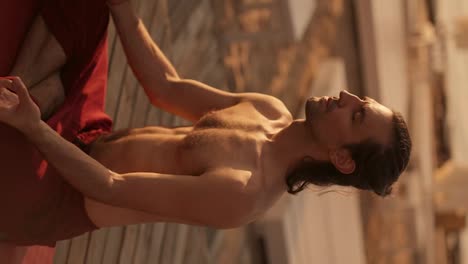 Vertical-video:-a-brunette-guy-with-a-naked-torso-in-red-pants-is-meditating-with-his-eyes-closed-on-a-sunny-beach-in-the-summer.-Zen-style-on-the-beach-in-summer