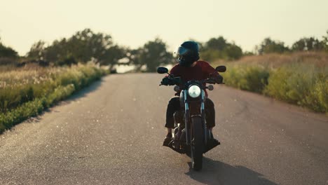 A-motorcyclist-in-a-red-jacket-and-in-a-helmet-is-riding-on-a-road-in-sunny-weather-with-a-breeze