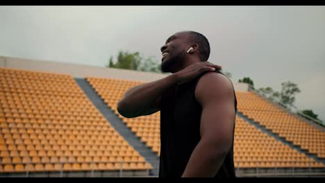 A-Black-man-in-black-sportswear-walks-through-the-stadium-and-stretches-his-joints-after-strength-training