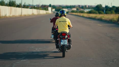 Fahrlehrer-Auf-Moped-Im-Gelben-T-Shirt-Folgt-Seinem-Fahrschüler-Im-Roten-T-Shirt-Auf-Breiter-Straße