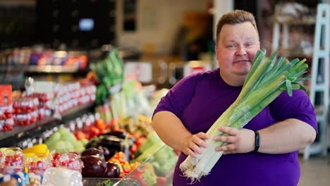 Portrait-of-a-Happy-and-joyful-overweight-man-in-a-purple-T-shirt-who-holds-a-bunch-of-shallots-in-his-hands,-sniffs-them-and-smiles-in-a-large-supermarket