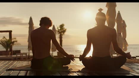 Zwei-Männer-Sitzen-Morgens-Auf-Einem-Speziellen-Teppich-Und-Meditieren-Am-Strand.-Zen-Stil-Bei-Sonnenaufgang