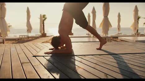 The-guy-stands-on-his-head-on-a-special-mat-on-a-sunny-beach.-Yoga-classes