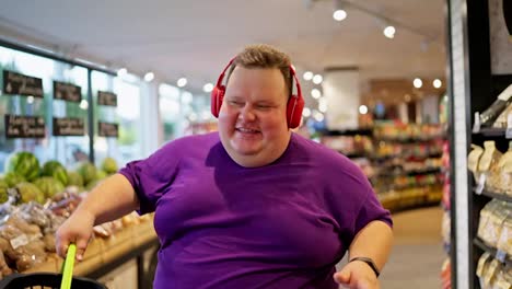 A-happy-man-in-a-purple-T-shirt-and-red-headphones-dances-and-walks-along-the-counters-in-a-large-supermarket.-Close-up-shot-of-a-happy-overweight-man-dancing-in-a-supermarket