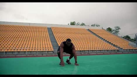 A-Black-man-in-black-sportswear-doing-a-burpee-exercise-in-a-stadium-with-yellow-stands