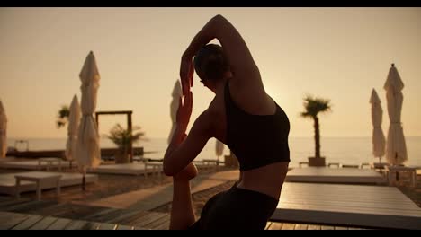 A-girl-in-a-black-summer-sports-uniform-does-stretching-and-takes-a-special-yoga-pose-on-a-red-mat-during-a-golden-sunset-in-the-evening-on-a-Sunny-beach