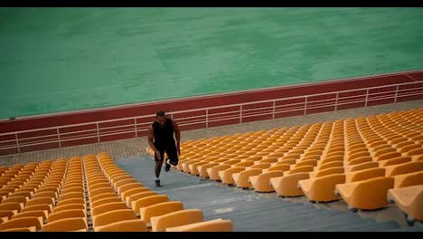 An-athlete-with-Black-skin-in-a-black-sports-summer-uniform-runs-in-the-upstairs-stands-of-the-stadium-with-yellow-chairs-on-it
