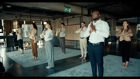 Das-Team-Im-Büro-Beschäftigt-Sich-Mit-Meditation-Und-Yoga.-Büroangestellte-Stehen-Im-Büro-Auf-Dem-Teppich-Und-Falten-Vor-Sich-Die-Hände