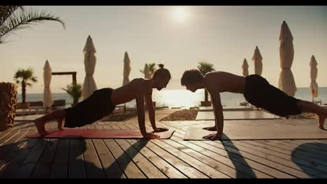 Zwei-Männer-Machen-Morgens-Yoga-Auf-Einem-Holzboden-Am-Strand.-Yoga-Kurse-Und-Zen-Stil