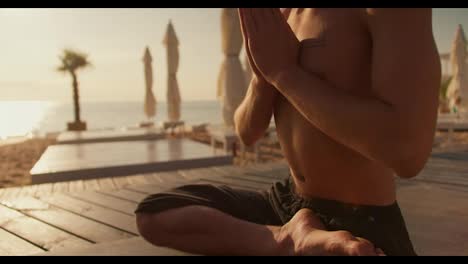 Close-up-shot:-a-view-of-a-calm-guy-meditating-on-the-beach-at-sunrise.-Morning-meditation-outdoors.-Harmony-of-body-and-mind