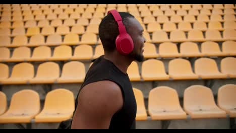 Portrait-of-a-young-athlete-with-Black-skin-color-in-a-black-shirt-and-red-wireless-headphones,-who-walks-under-the-stadium-with