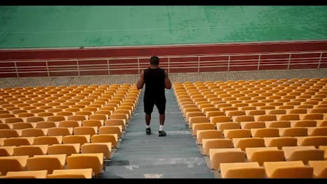 Athletic-man-in-black-sportswear-runs-down-the-stairs-of-the-stadium-stand-with-yellow-chairs