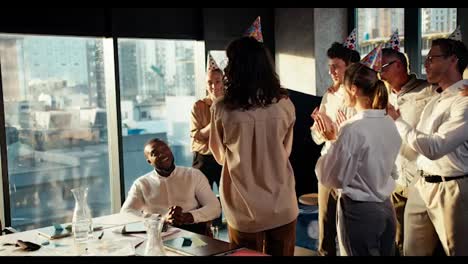 Congratulation-Black-male-businessman-in-a-business-team-at-work-in-the-office.-Colleagues-in-festive-hats-brought-a-cake-with