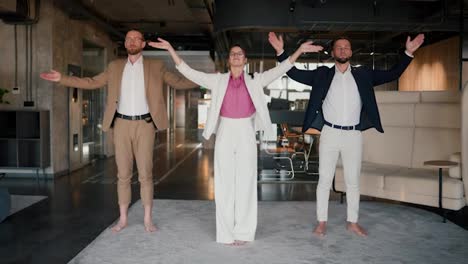 Portrait-of-three-office-workers-who-are-standing-on-the-carpet-doing-meditation-in-the-office-during-a-break.-Harmony-with-yourself-while-working