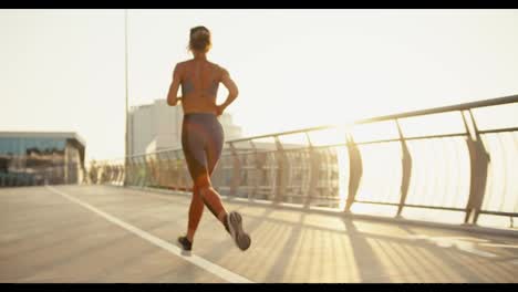 Rear-view-of-a-young-athletic-girl-in-a-sports-summer-uniform-jogging-in-the-morning.-sunrise-sun-rays
