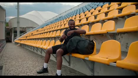 A-Black-skinned-athlete-in-a-black-sports-summer-uniform-takes-out-a-special-bottle-of-water-from-his-bag-and-drinks-it-in-the