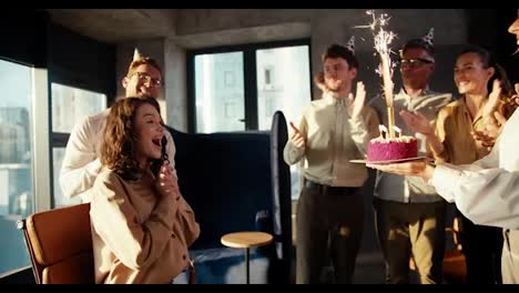 Colleagues-made-a-surprise-for-a-business-girl-in-a-brown-shirt-and-brought-her-a-cake-with-candles.-The-girl-is-very-happy-with
