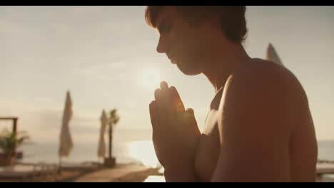Close-up-shot:-a-view-of-a-calm-guy-meditating-on-the-beach-at-sunrise.-Morning-meditation-outdoors