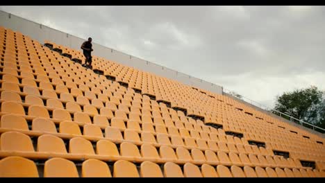 An-athlete-with-Black-skin-color-in-black-sports-summer-clothes-goes-down-the-stairs-in-the-stadium-with-yellow-chairs-in-the