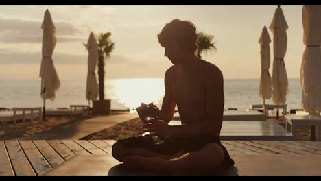 The-guy-takes-a-bottle-of-water-and-drinks-on-a-sunny-beach-in-the-morning.-Relaxation-and-relaxation-on-the-beach-at-sunrise