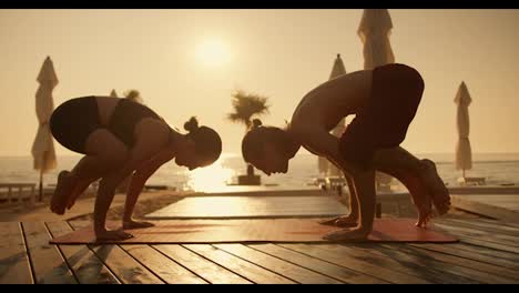 A-guy-and-a-girl-are-doing-yoga-and-doing-a-bird-pose-on-a-red-mat-on-a-Sunny-beach-during-sunrise.-Combination-of-acrobatics