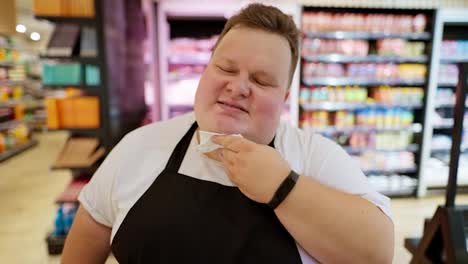 A-tired-supermarket-worker,-Overweight-man,-in-a-white-T-shirt-and-a-black-apron-wipes-sweat-from-his-forehead-with-a-white-napkin.-Taking-a-break-during-a-hard-day-at-work