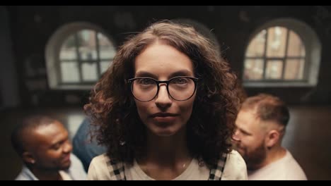 Portrait-of-a-brunette-girl-with-curly-hair-in-glasses-who-looks-at-the-camera-and-then-falls-into-the-arms-of-her-friends-during-group-therapy-and-trust-practice
