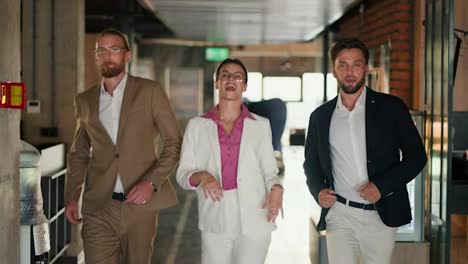Happy-3-office-workers:-A-brunette-girl-in-round-glasses-and-a-white-jacket-in-a-pink-shirt-walks-with-her-colleagues-and-guys-in-the-office-and-dances