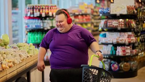 A-happy-man-in-a-purple-T-shirt-and-red-headphones-walks-through-the-supermarket-and-listens-to-music-while-shaking-his-head.-A-fun-trip-to-the-supermarket-while-listening-to-music