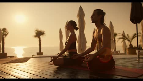 Ein-Paar,-Ein-Mann-Und-Ein-Mädchen,-Meditieren-Während-Eines-Goldenen-Sonnenaufgangs-Im-Sommer-Auf-Einem-Roten-Teppich-An-Einem-Mit-Brettern-Bedeckten-Strand