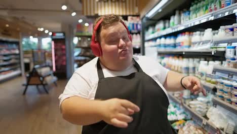 Happy-male-supermarket-worker-with-overweight-white-T-shirt-and-black-front-in-red-headphones-is-happy-dancing-and-walking-along-the-milk-aisles-in-the-supermarket