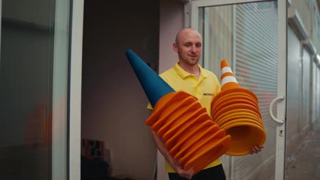 A-bald-man-with-blue-eyes-in-a-yellow-T-shirt-takes-orange-cones-out-of-his-garage-for-a-training-ground-in-a-motorcycle-school