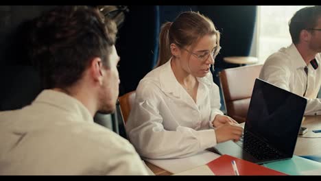 a-blonde-girl-in-glasses-in-a-white-shirt-shows-her-project-on-a-laptop-to-a-manager-in-a-white-shirt