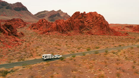 Drone-shot-tracking-a-camper-trailer-on-a-road-in-middle-of-red-desert-in-NV,-USA