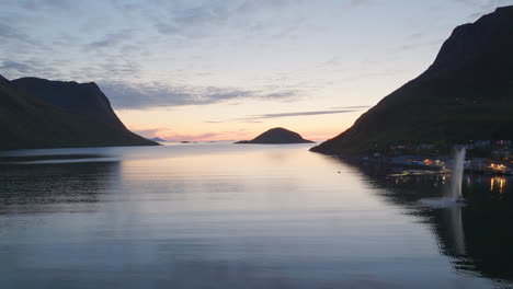 Aerial-dolly-above-idyllic-coastal-village-of-Torsken-Norway-at-sunset,-reflection-on-ocean