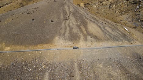Aerial-drone-following-shot-of-a-car-passing-sand-mountain-in-Spiti-valley,-Himachal-Pradesh,-India