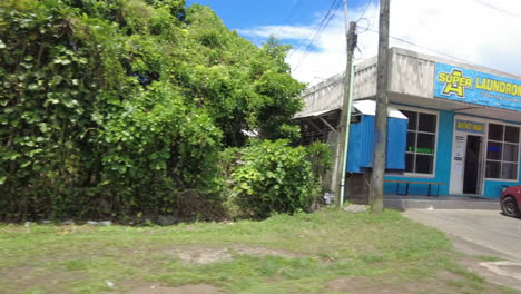 POV-out-the-window-driving-past-streets-and-buildings-in-Apia,-Samoa