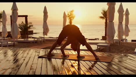 The-guy-gets-on-his-head-in-a-special-yoga-exercise-on-the-beach-in-the-morning.-Yoga-classes-at-dawn-healthy-lifestyle
