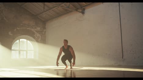 A-guy-in-a-black-sports-summer-uniform-does-a-burpee-exercise-on-the-Red-Mat-in-the-Sunny-Brick-Hall