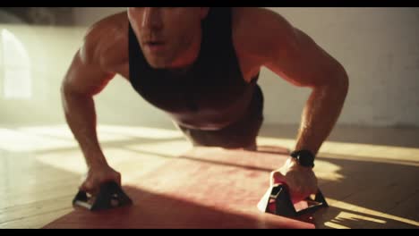 Close-up-shot-of-a-man-in-a-black-T-shirt-doing-push-ups-using-special-handrests-on-a-red-mat