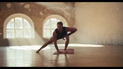 Male-gymnast-doing-fitness-in-the-solar-hall.-Sports-and-gymnastics-warm-up-for-muscle-stretching-and-strengthening.-A-guy-in-black-sportswear-goes-in-for-sports-in-a-sunny-gym