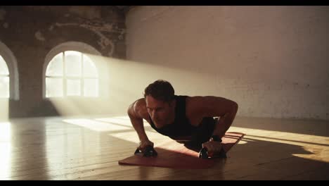 Close-up-shot-of-a-man-in-black-sportswear-summer-uniform-doing-push-ups-using-special-hand-rests-on-the-Red-Mat-in-the-Sunny