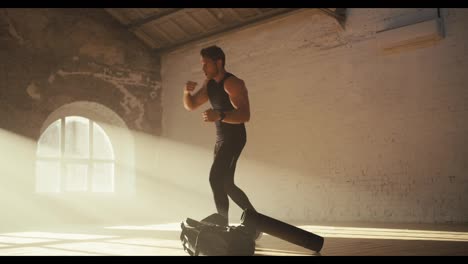 A-man-in-a-black-summer-sports-uniform-is-engaged-in-fitness-and-practice-boxing-punches-in-a-sunny-brick-gym